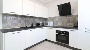 A modern kitchen with white cabinets, a black countertop, a microwave, a coffee maker, and a built-in oven. - Benedetta Suite in Florence (Florence)