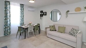 A modern living room with a dining area, a round mirror, and a sofa with cushions. - Benedetta Suite in Florence (Florence)