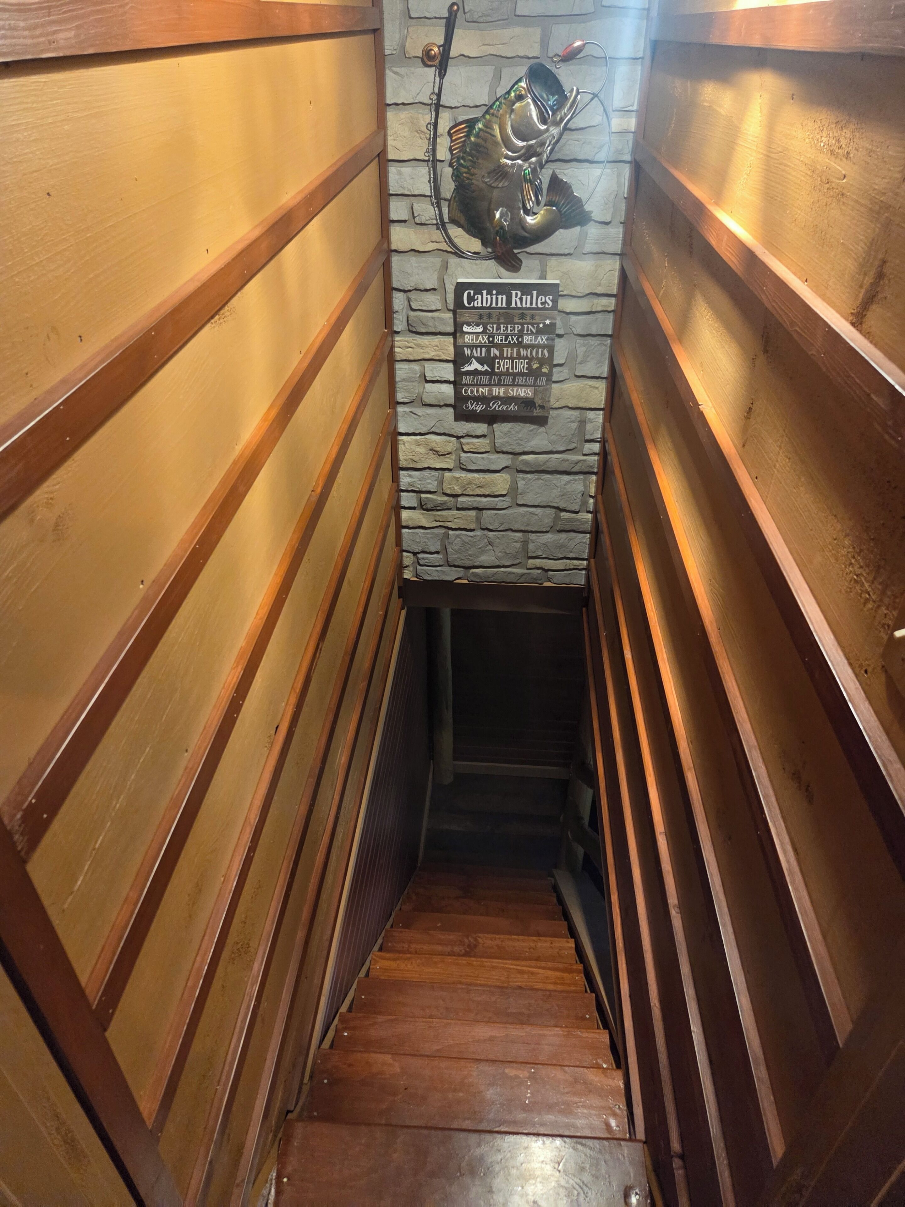 Una escalera de madera con un muro de piedra y un letrero que dice 'Cabin Rules'.