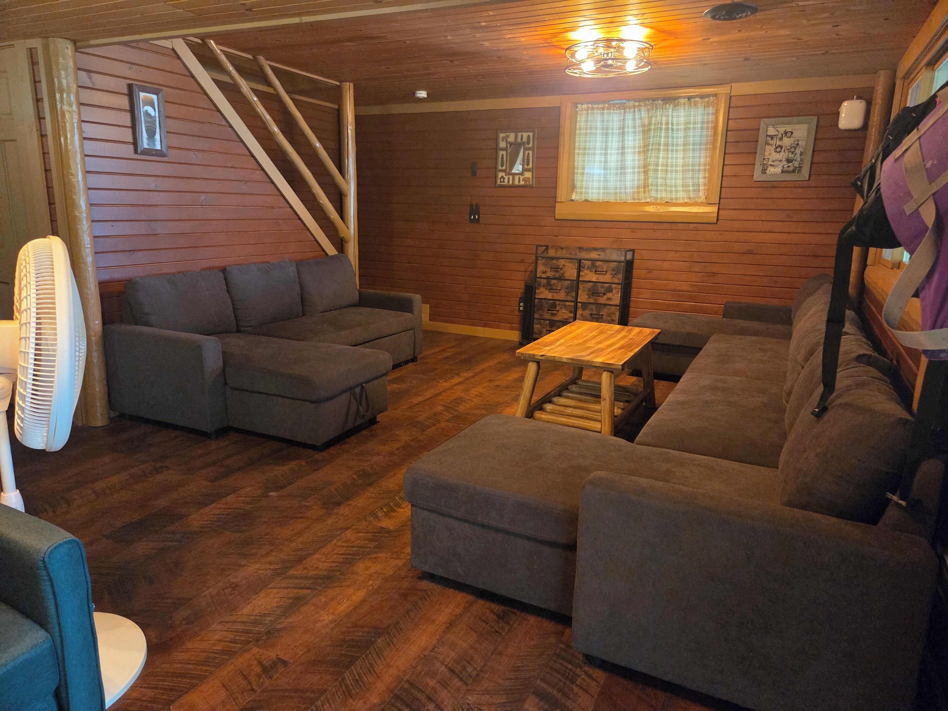 A cozy living room with a wooden floor, grey sofas, a wooden coffee table, and a fan.