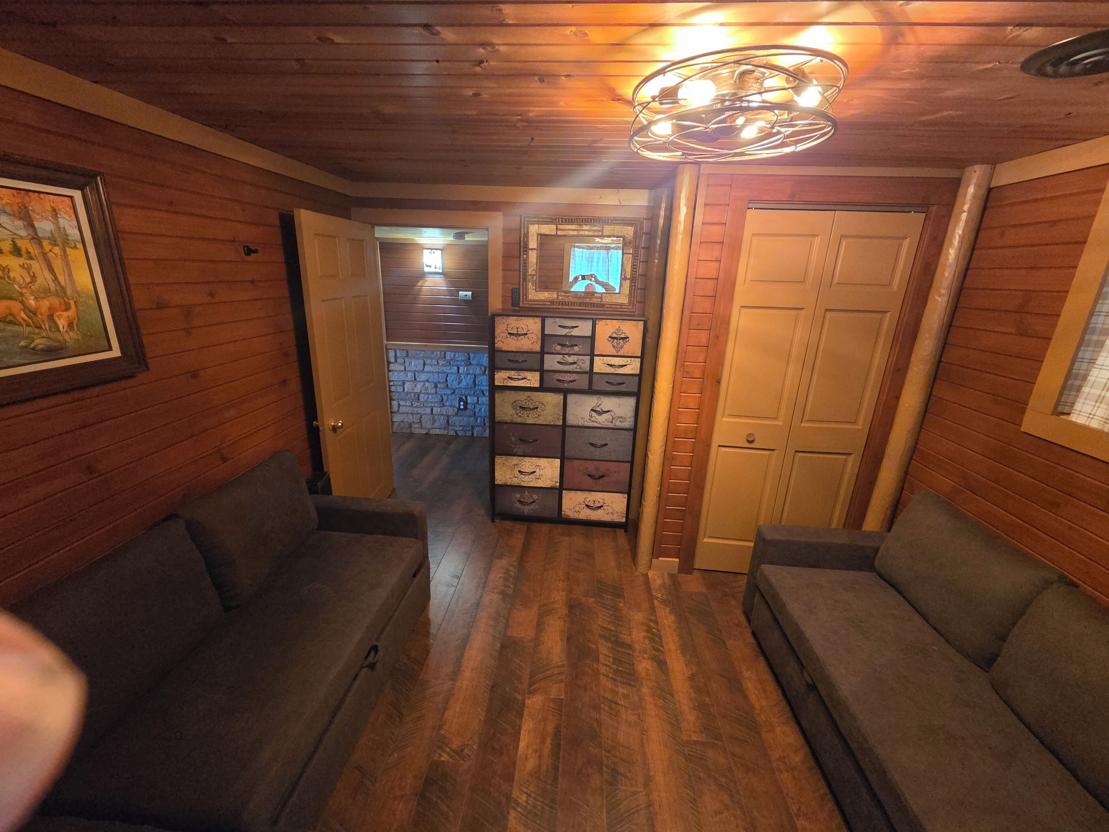 Interior em madeira com corredor, dois sofás, um armário suspenso com gavetas e um lustre.