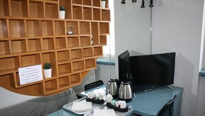 Una camera d'albergo con un mobile contenitore in legno, una scrivania con computer, una macchina per il caffè e una TV.