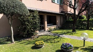 Un edificio con una zona salotto esterna coperta, un prato curato e aiuole fiorite.