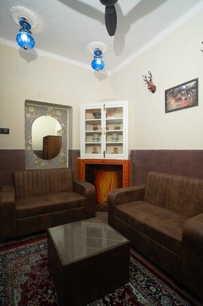 A living room with two brown sofas, a glass coffee table, a fireplace, a decorative mirror, and a cabinet with glass doors. - L2 Darbar Kothi (Jodhpur)