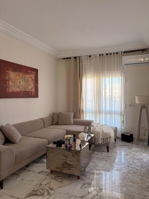 A living room with a sofa, a coffee table, and a painting on the wall. - A cozy little apartment just a stone's throw from the ocean (Hammamet)