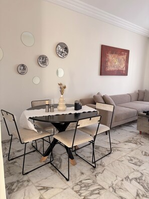 A dining area with a round table, chairs, and a vase of dried flowers. - Cosy little apartment a stone's throw from the sea (Hammamet)