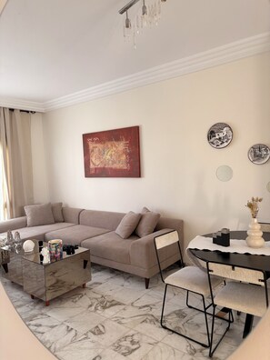 A modern living room with a sofa, coffee table, and a dining area with chairs and a table. - A cozy little apartment just a stone's throw from the ocean (Hammamet)