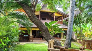 A traditional wooden building with a thatched roof, surrounded by lush greenery and a well-maintained lawn. - Romantic Joglo Villa Near Lovina Beach & Center (Buleleng)