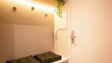 Quarto de hotel com mesa de cabeceira, travesseiro verde, luminária de cabeceira, telefone e luminária na parede.