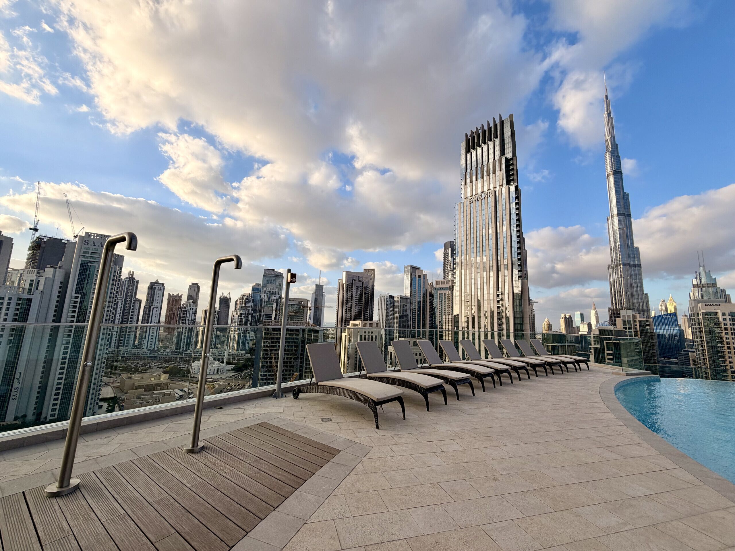 A rooftop terrace with lounge chairs and a swimming pool, overlooking a cityscape with modern skyscrapers.