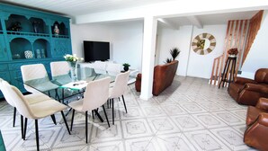 A modern living room with a glass dining table, beige chairs, a TV, and a patterned floor.
