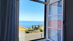 A window with a view of the sea, a tiled roof, and a fence.
