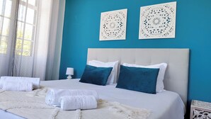 A hotel room with a bed, two pillows, a white headboard, a white lamp, and two wall art pieces.