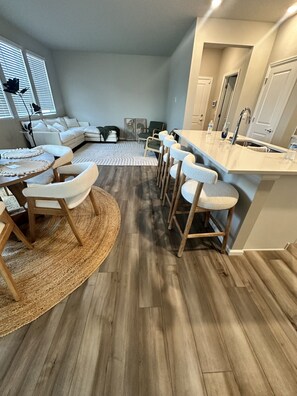 A modern kitchen with a bar area, wooden flooring, and a dining set.