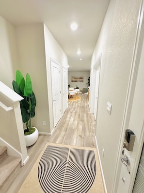 A hallway with a wooden floor, white walls, a potted plant, and a patterned rug.