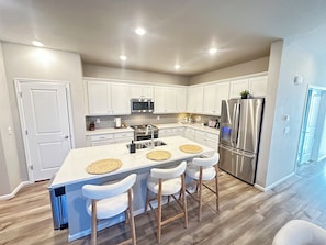A modern kitchen with white cabinets, stainless steel appliances, a central island with stools, and a wooden floor.