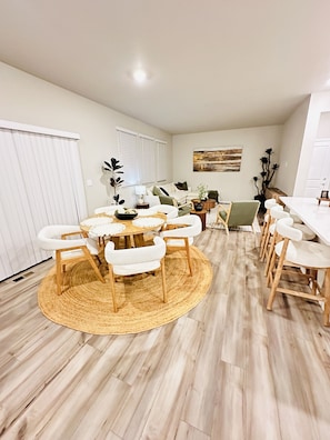 A dining area with a round wooden table, white upholstered chairs, and a woven rug.