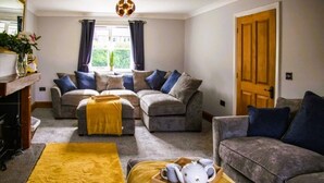 A living room with two grey sofas, a yellow rug, and a wooden door. - 4 Bed House Sleeps 10 - Pets, Parking, Games Room (Filey)