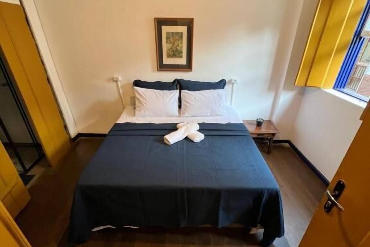 A hotel room with a bed, a bedside table, a window, and a door.