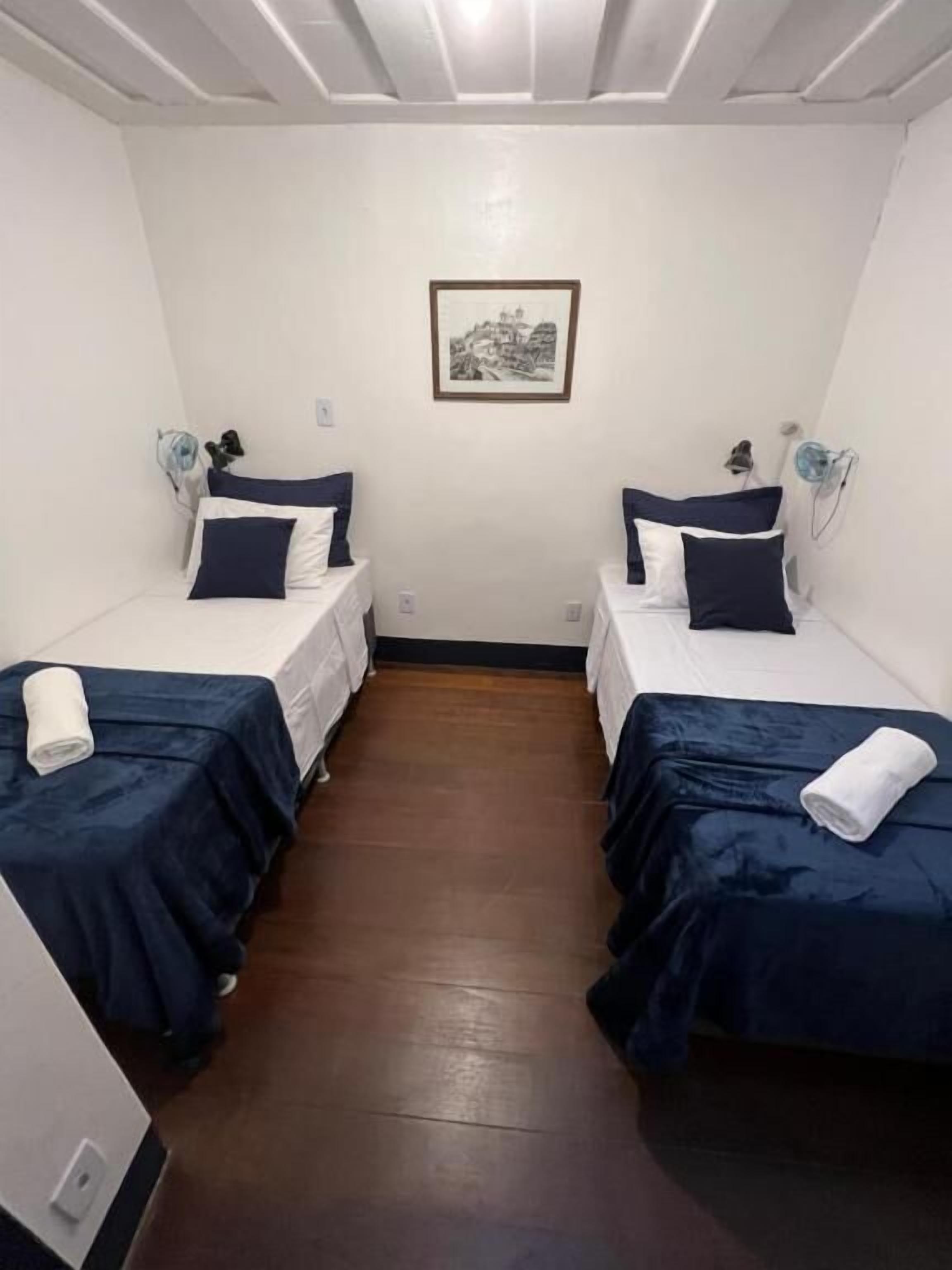Una habitación con dos camas, cada una con una colcha azul oscuro y almohadas blancas, un cuadro en la pared y suelo de madera.