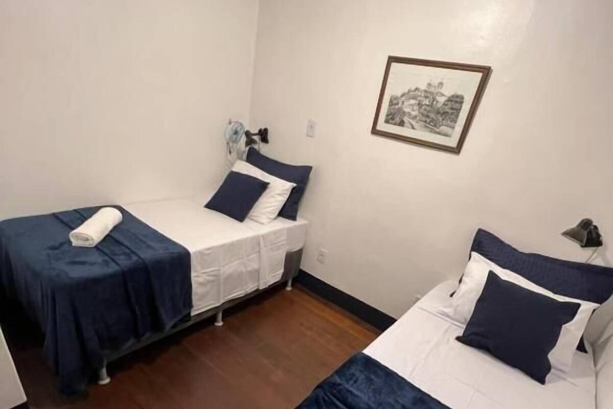 A room with two beds, each with a blue bedspread and white linens, a framed picture on the wall, and a wooden floor.