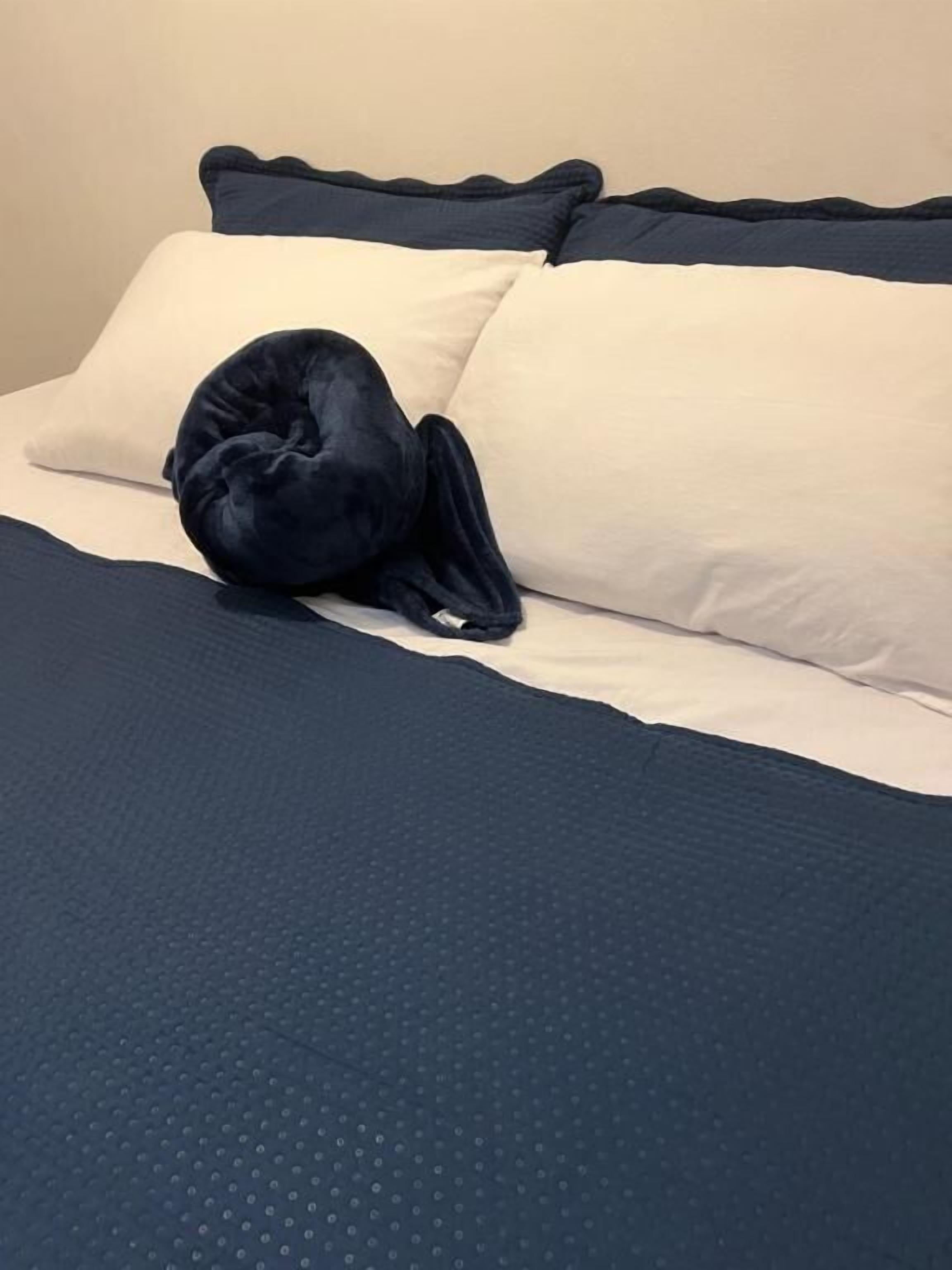 A bed with a dark blue bedspread and pillows, a dark blue blanket, and a dark blue pillow.