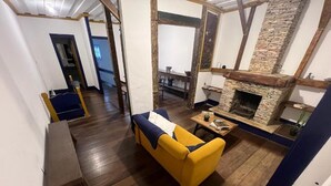 A room with a yellow sofa, a stone fireplace, wooden beams, and a wooden floor. - History Hostel (Ouro Preto)