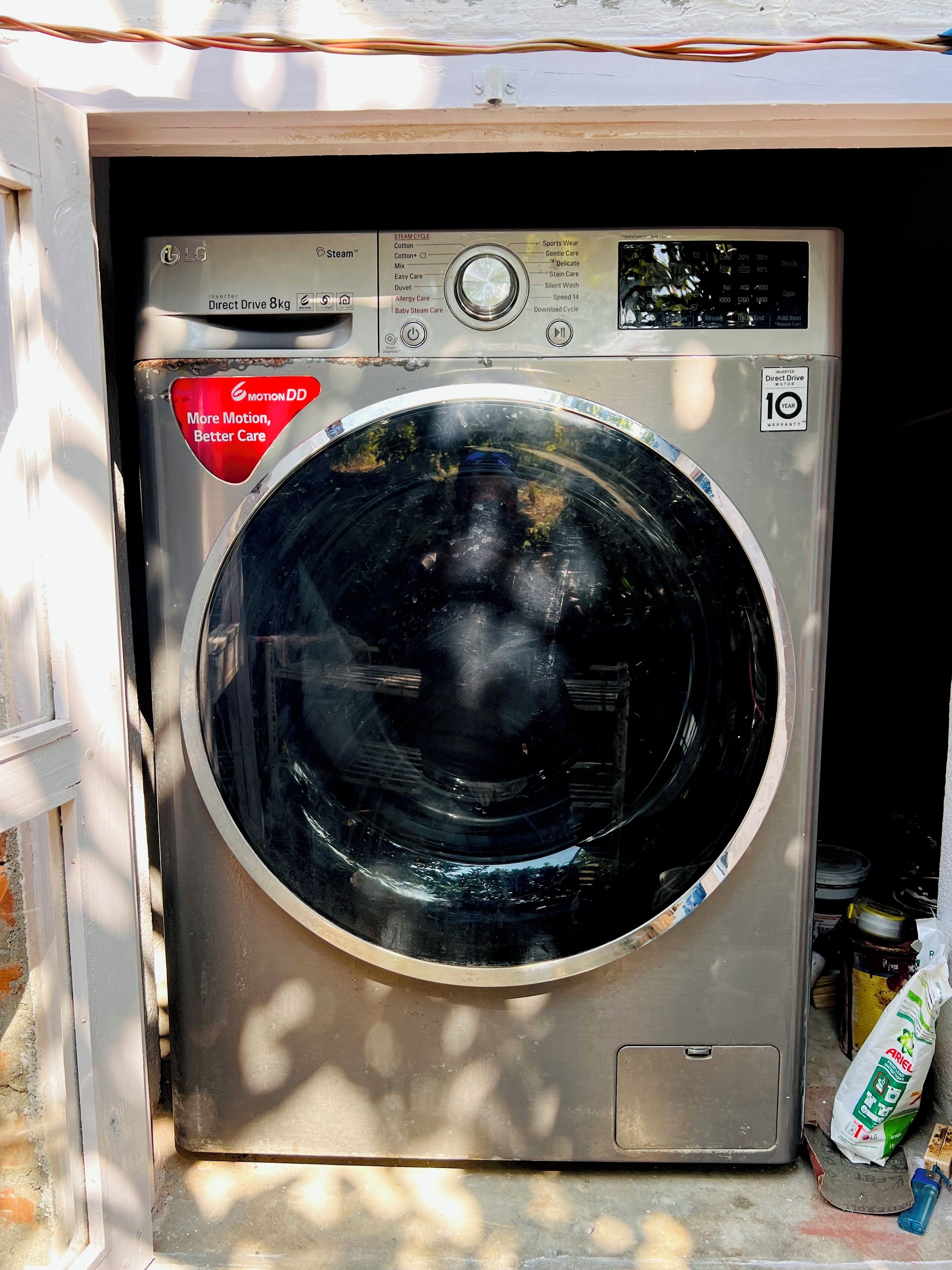 A front-loading washing machine with a stainless steel exterior, a control panel with various settings, and a 10-year warranty sticker.
