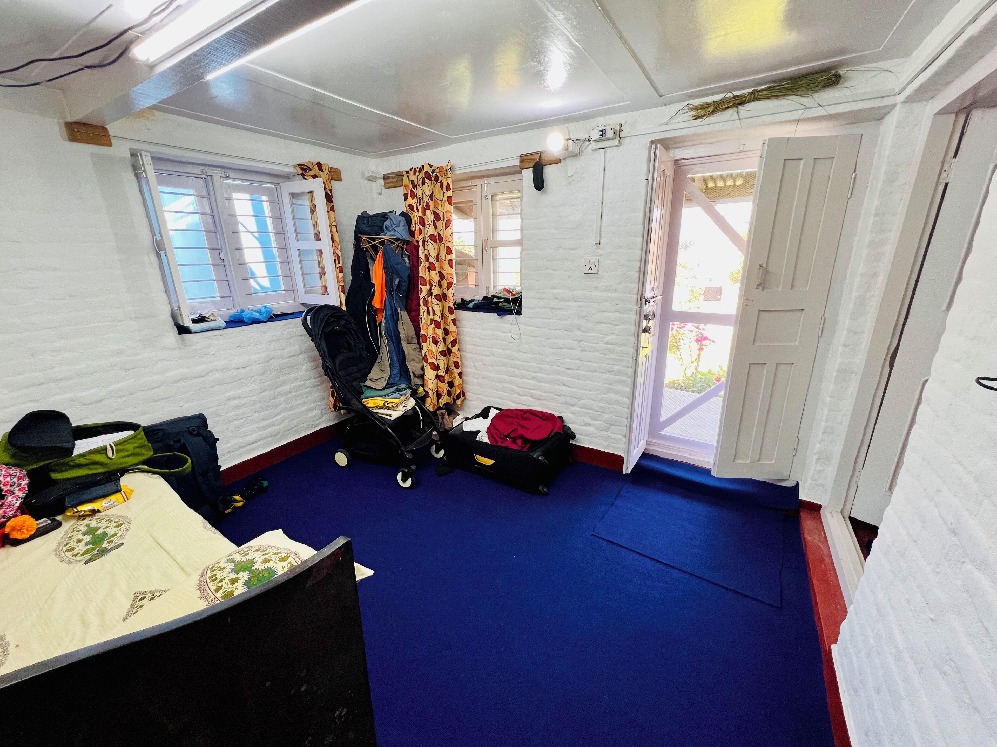 Een kamer met een bed, een koffer, een kinderwagen en een raam met gordijnen.