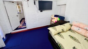 Un dormitorio con una cama, un televisor montado en la pared y una puerta que da a otra habitación.