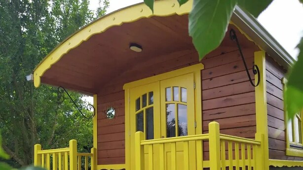 Une cabane en bois aux boiseries jaunes, dotée d’un porche et d’une petite terrasse.