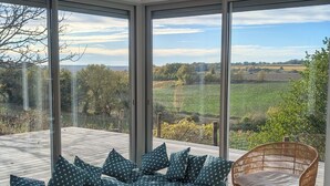 Un salon moderne avec de grandes fenêtres, une table ronde en bois et un fauteuil en osier.