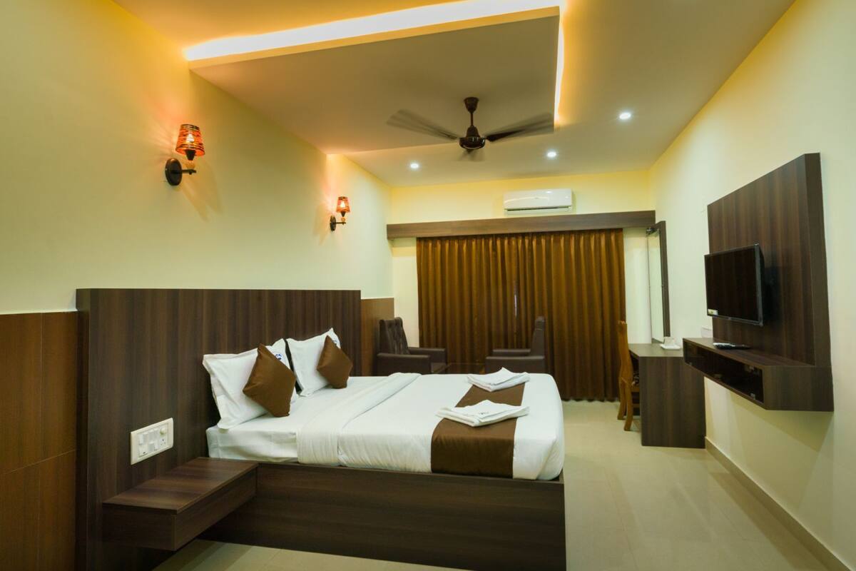 A hotel room with a bed, bedside tables, a desk, a chair, a TV, and a ceiling fan.