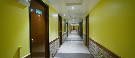 A hotel corridor with yellow walls, a tiled floor, and doors leading to rooms.