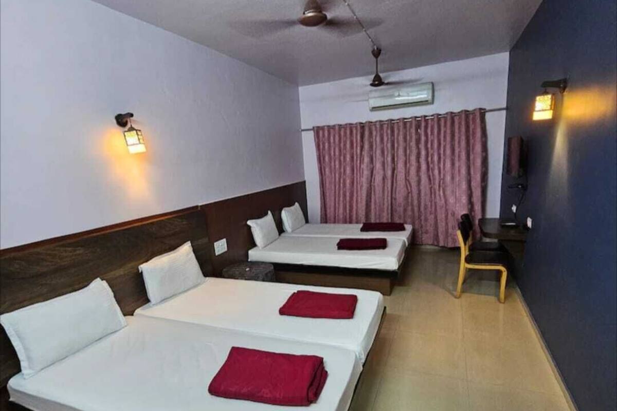 A hotel room with three single beds, a ceiling fan, an air conditioning unit, and a small seating area with a chair.
