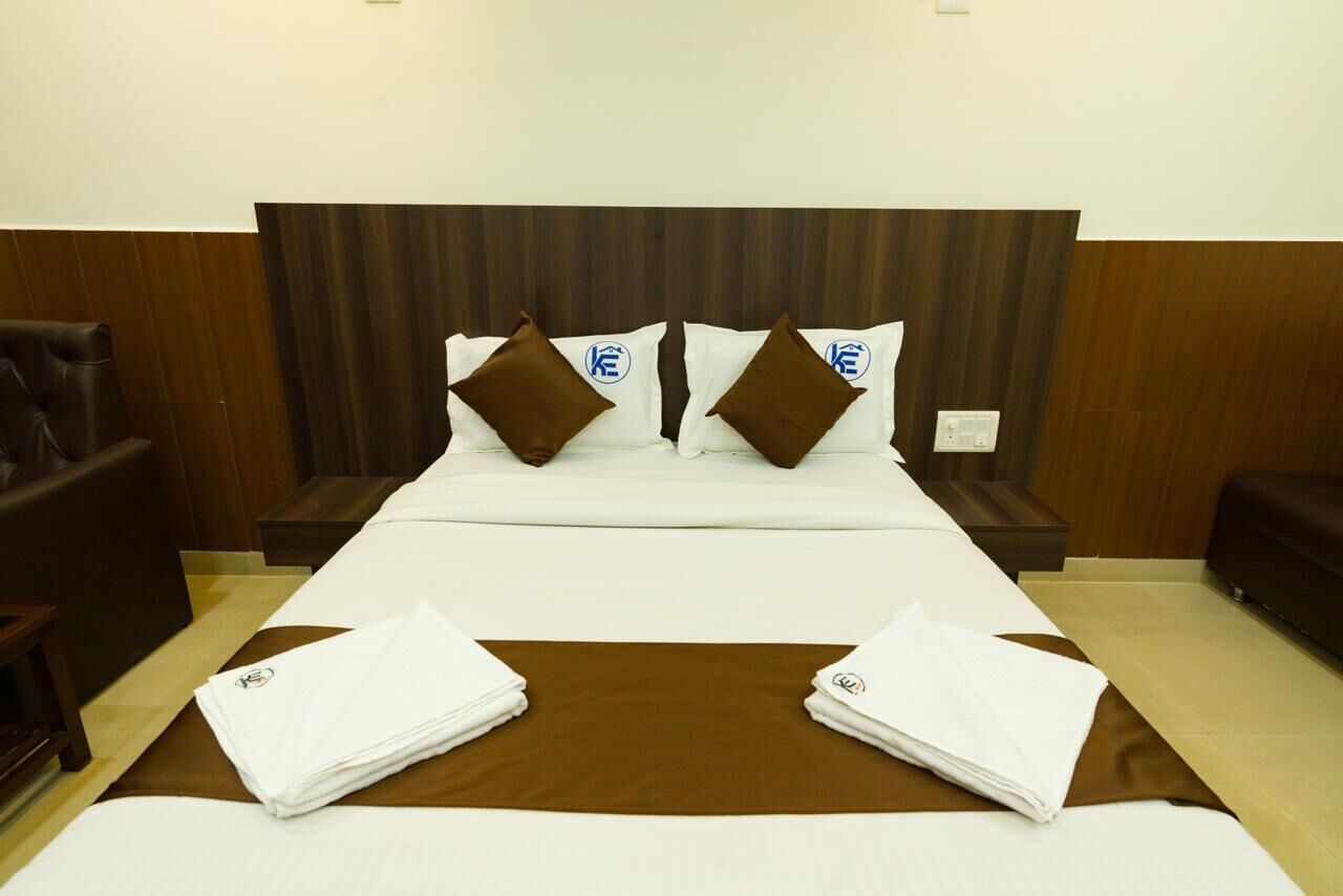 A hotel room with a large bed, two pillows with a logo, a brown throw blanket, and a folded white towel.