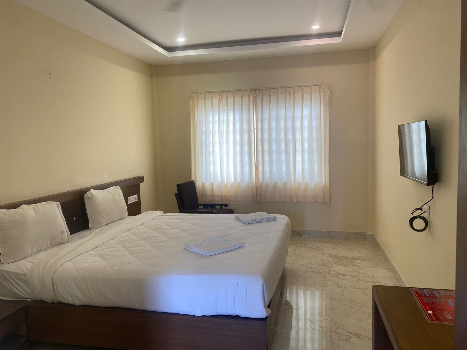 Une chambre d’hôtel avec un grand lit, un bureau, une chaise, une télévision et une fenêtre avec des rideaux.