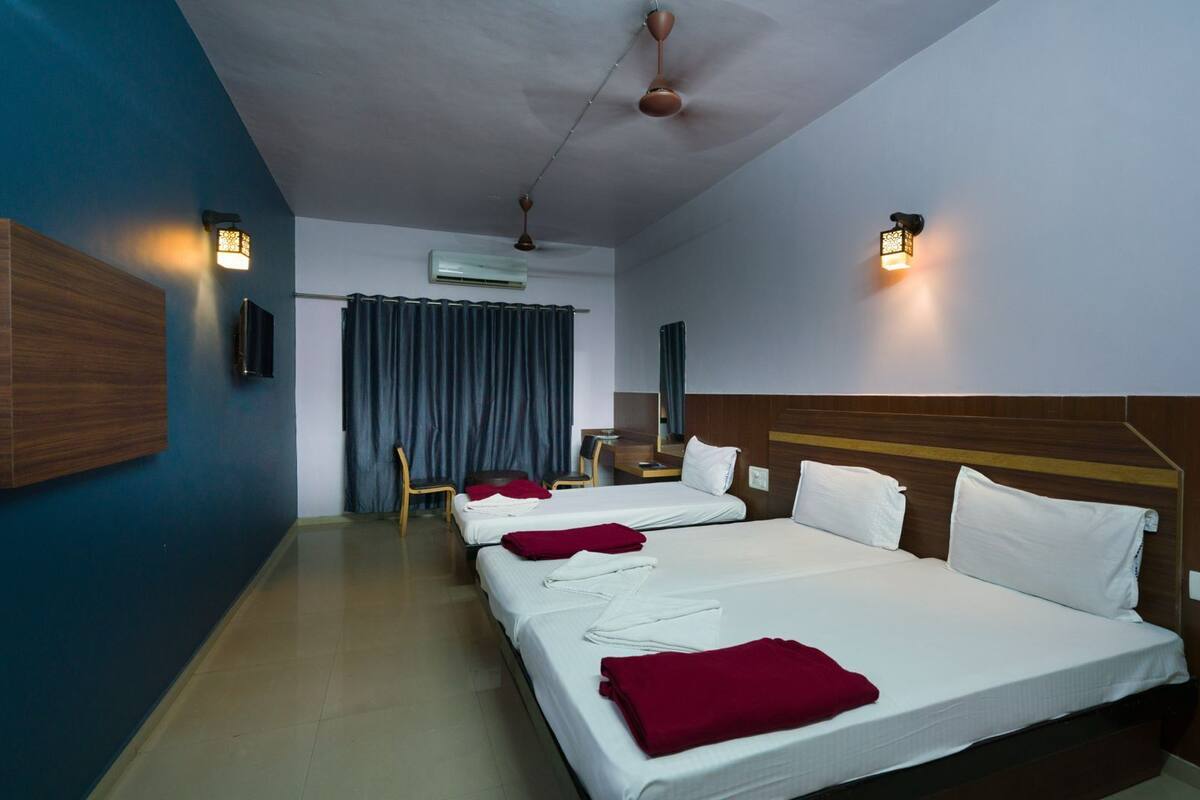 A hotel room with two beds, a ceiling fan, wall-mounted lights, an air conditioning unit, and a wooden headboard.