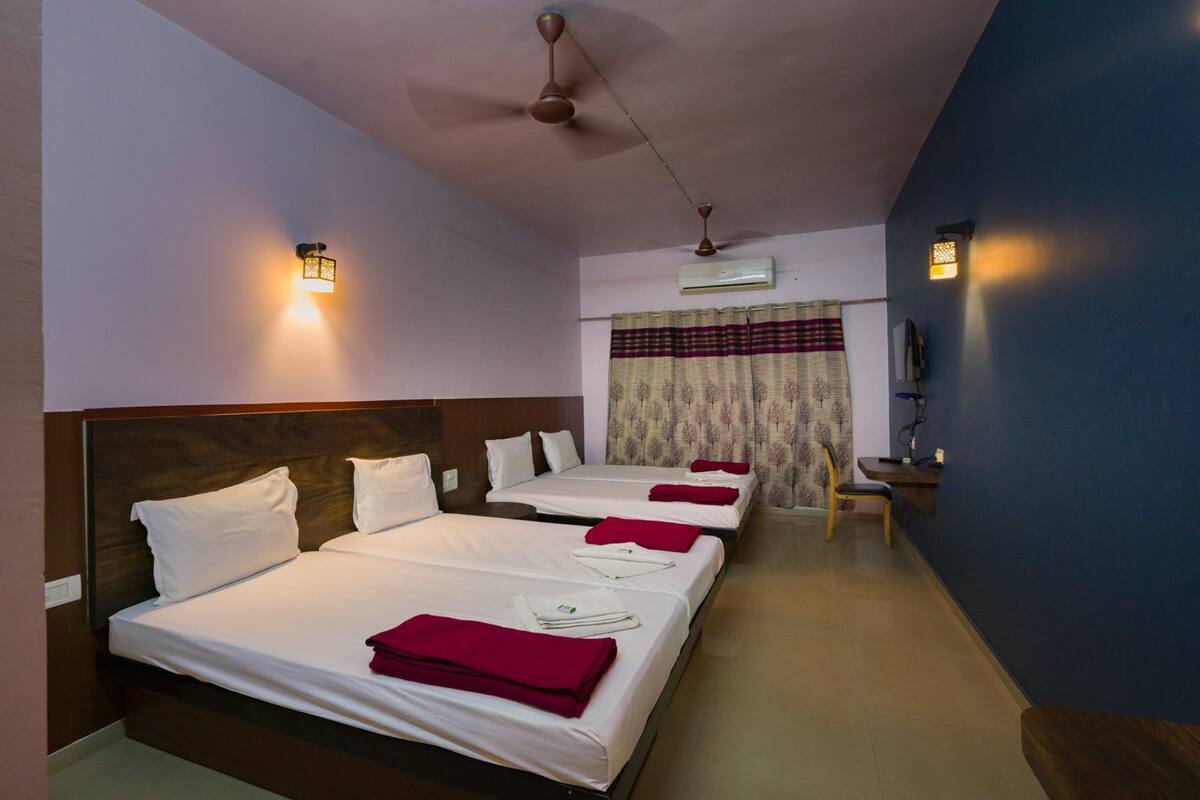 A hotel room with three beds, a ceiling fan, an air conditioning unit, and a television on a wooden stand.