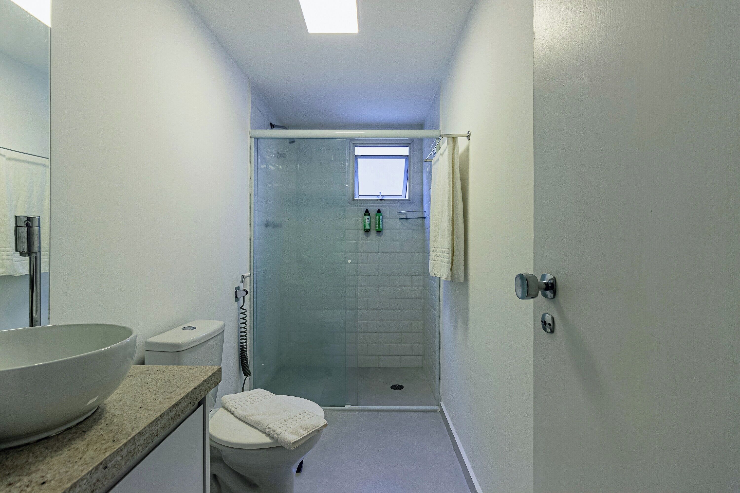 Une salle de bain dotée d’une douche à parois de verre, de toilettes, d’un lavabo avec un grand bac et d’une fenêtre située au-dessus de la douche.