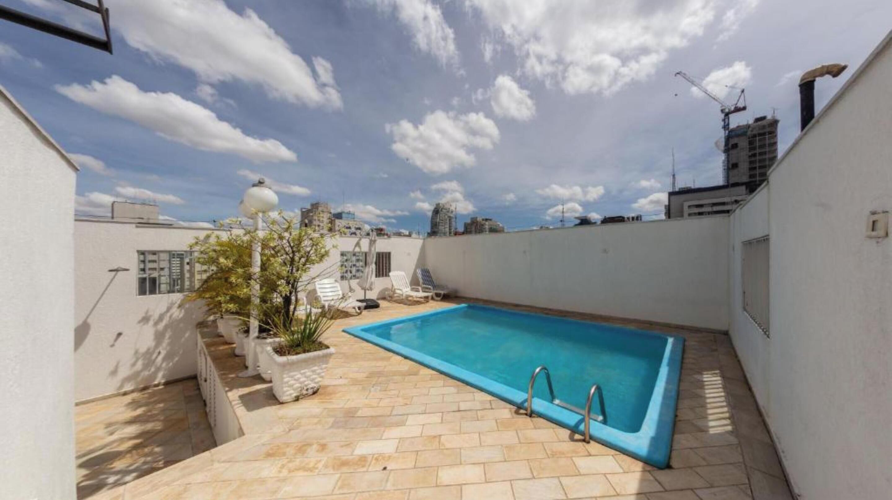 Una piscina en la azotea, de aguas azules cristalinas, rodeada de plantas en macetas y algunas sillas de descanso.