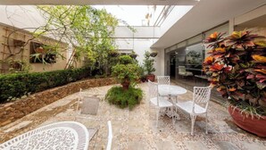 Eine Terrasse im Freien mit Steinboden, weißen Korbmöbeln und verschiedenen Topfpflanzen.