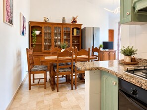 A compact kitchen with a dining area, featuring a granite countertop, wooden cabinets, and a built-in stove. - Capo Comino 1 - Two Bedroom Apartment, Sleeps 5 (La Caletta)