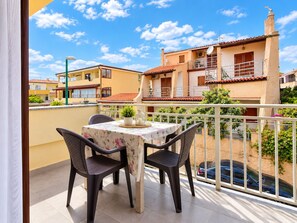 A balcony with a table and chairs, a view of neighboring buildings, and a clear sky. - Capo Comino 1 - Two Bedroom Apartment, Sleeps 5 (La Caletta)