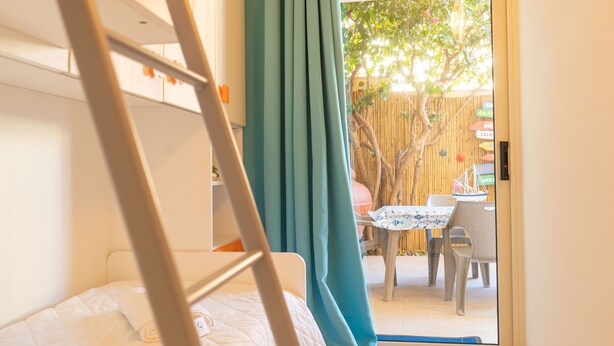Una habitación con cama, ventana con cortinas y vistas a una mesa y sillas al aire libre.