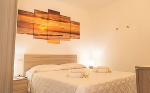 A hotel room with a bed, a nightstand, a lamp, and a wall-mounted artwork. - Bouganville - Two Bedroom Apartment, Sleeps 4 (Posada)