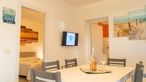 Una habitación de hotel con cama, televisión, mesa de comedor con sillas y un cuadro con motivos playeros.