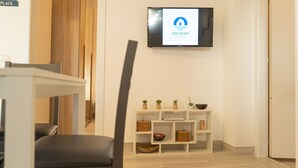 Un moderno vestíbulo de hotel con un televisor de pantalla plana mostrando un logo, un mostrador de recepción, una zona de estar y una pequeña exhibición de plantas.