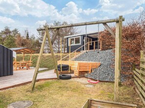 A wooden deck with a swing set, a picnic table, and a small building with a dark exterior. - 4 Star Holiday Home in Ebeltoft (Ebeltoft)