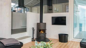 Una sala de estar moderna con una chimenea de leña, un televisor de pantalla plana montado en la pared y un ventanal grande.